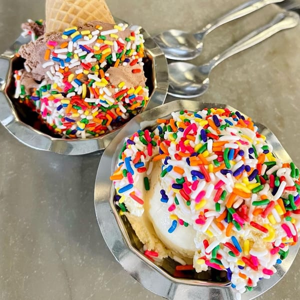 Two Hildebrandt's ice cream sundaes with colorful sprinkles, one chocolate and one vanilla, with spoons.