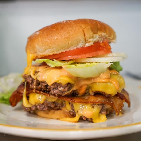 A towering double cheeseburger with bacon, lettuce, tomato, onion, and special sauce on a white plate.