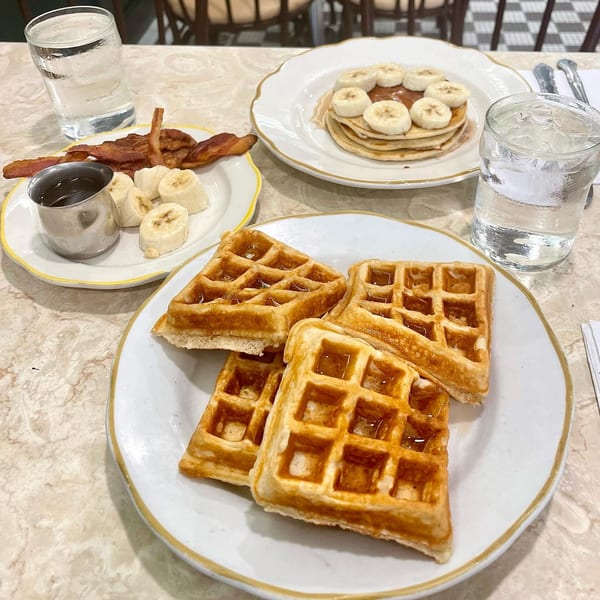 A breakfast spread featuring waffles, pancakes with bananas, bacon, and sliced bananas with syrup.