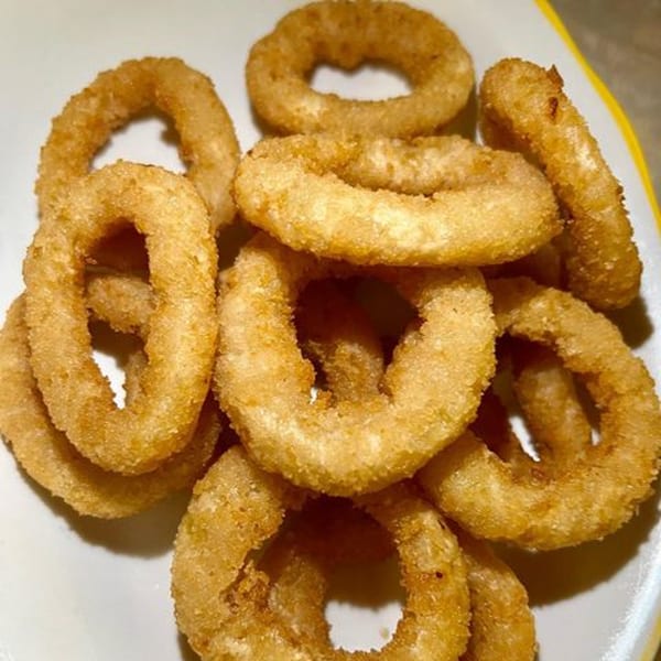A close-up of golden-brown, crispy onion rings piled on a white plate with a yellow rim.