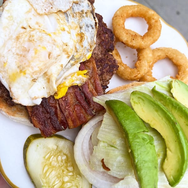 Hildebrandt's burger with a fried egg, bacon, avocado, lettuce, onion, pickle, and onion rings.