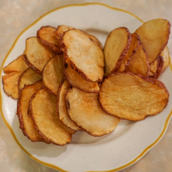 A white plate with a yellow rim filled with golden-brown, thinly sliced potato chips.