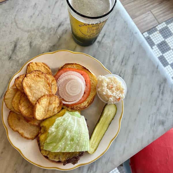 A Hildebrandt's burger with chips, coleslaw, and a pickle, next to a branded glass of beer.