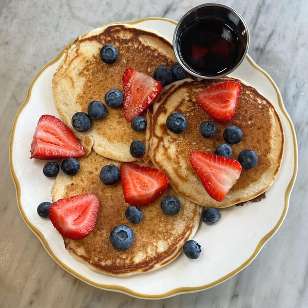 Pancakes topped with fresh blueberries and sliced strawberries, with a side of syrup.