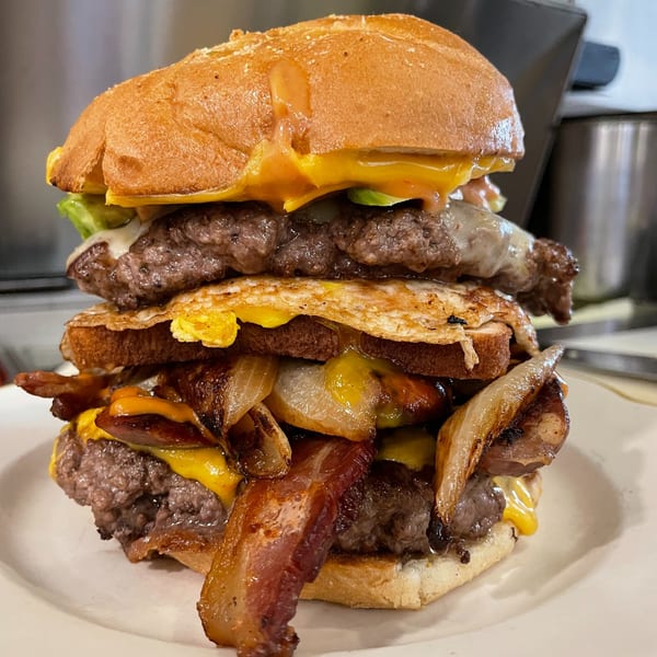 A towering Hildebrandt's burger with multiple patties, bacon, fried egg, cheese, and caramelized onions.